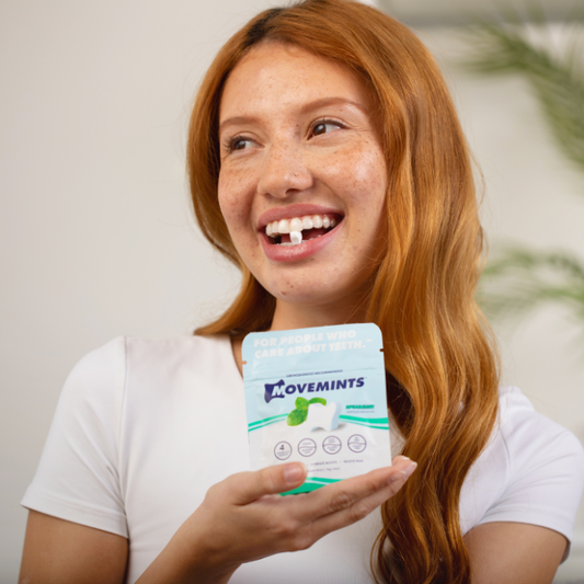 Red-haired model holding a bag of Spearmint Movemints and smiling with a Movemint between her teeth