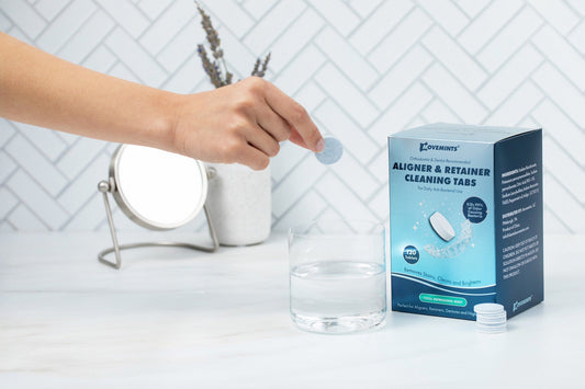 Box of Movemints Aligner & Retainer Cleaning Tabs and hand dropping tab into glass of water