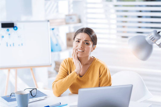 woman holding hand to face teeth pain in office