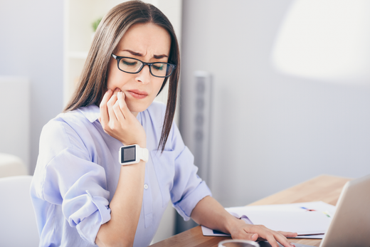 woman with glasses clutching mouth in pain